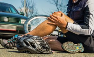 injured cyclist sitting on ground with bloody knee after accident