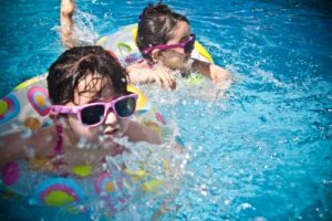 two young girls with sunglasses and tubes swimming in swimming pool