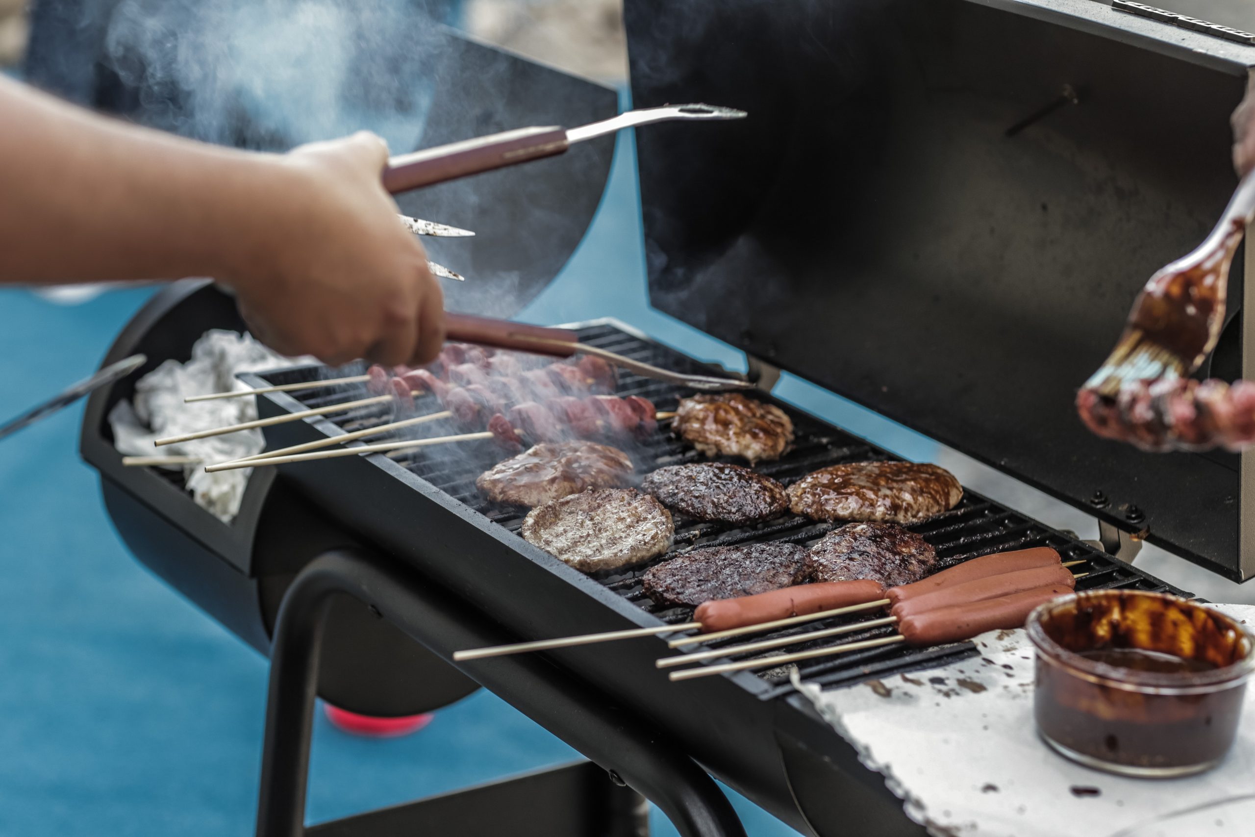 close up of cooking hamburgers and hot dogs on outdoor grill