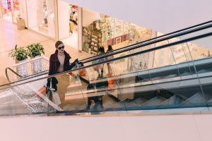 woman with shopping bags going up escalator in shopping mall