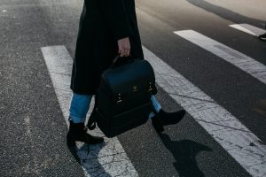 close up of woman carrying black backpack crossing street at crosswalk