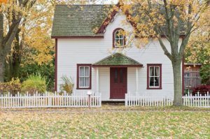 small quaint white house with red trim and picket fence