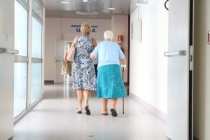 elderly woman walking with another woman helping her in a hospital hallway