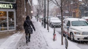 woman in black winter coat walking on snowy city sidewalk in winter