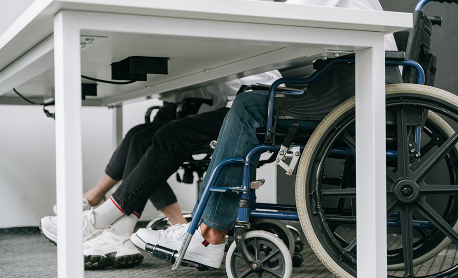 close up of two people sitting at desk, one in a wheelchair